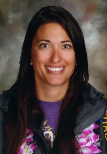 Portrait of a smiling woman with long dark hair, wearing a purple shirt and black jacket, against a blurred background