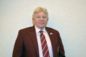 Man in a maroon suit and striped tie standing against a plain light background