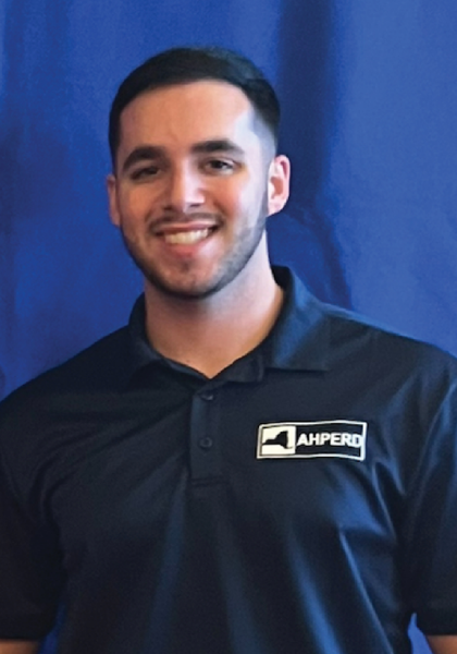 Smiling person in a black AHPERD polo standing before a blue backdrop.