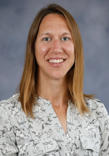 Smiling woman in a white patterned blouse against a gray studio background
