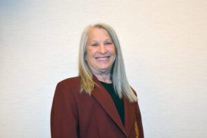 Smiling person in a maroon blazer standing against a plain light wall.