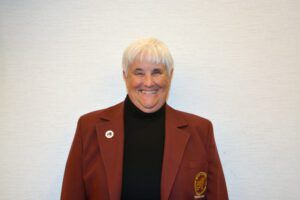 Smiling person in a red blazer with a black turtleneck standing against a plain light wall