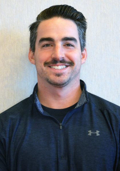 Smiling person with dark hair and mustache wearing a navy zip-up jacket against a light background