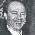Black-and-white close-up of a smiling man in a suit and tie