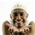 Smiling man in a white cap holding out both open hands toward the camera