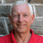 Smiling man in a red shirt in front of a brick wall