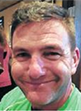 Smiling man in a green shirt, close-up portrait with a blurred indoor background