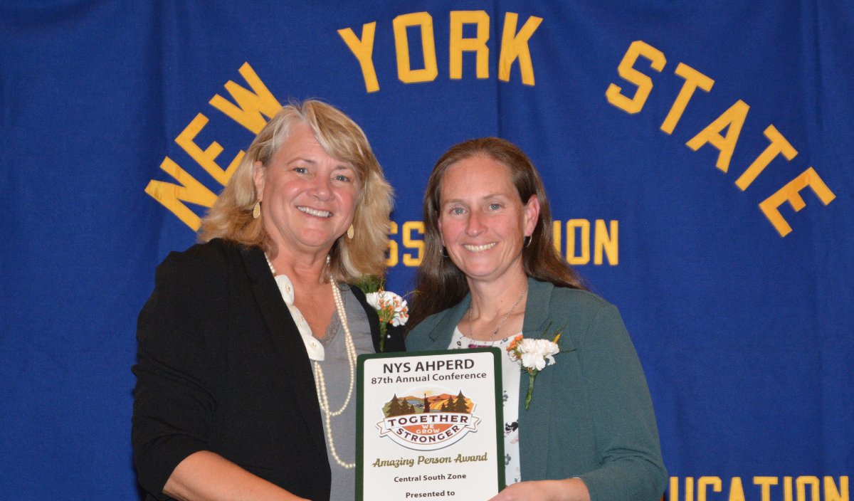 Two women holding a certificate in front of a New York State Education banner