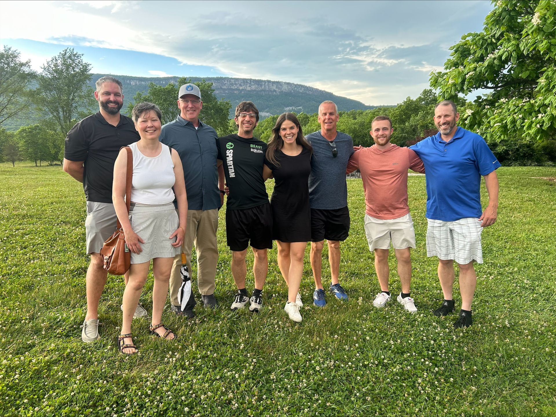 Seven people standing on a grassy field with hills and a blue sky in the background.