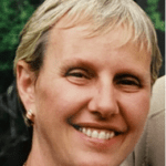 Close-up of a smiling person with short blond hair against a neutral background