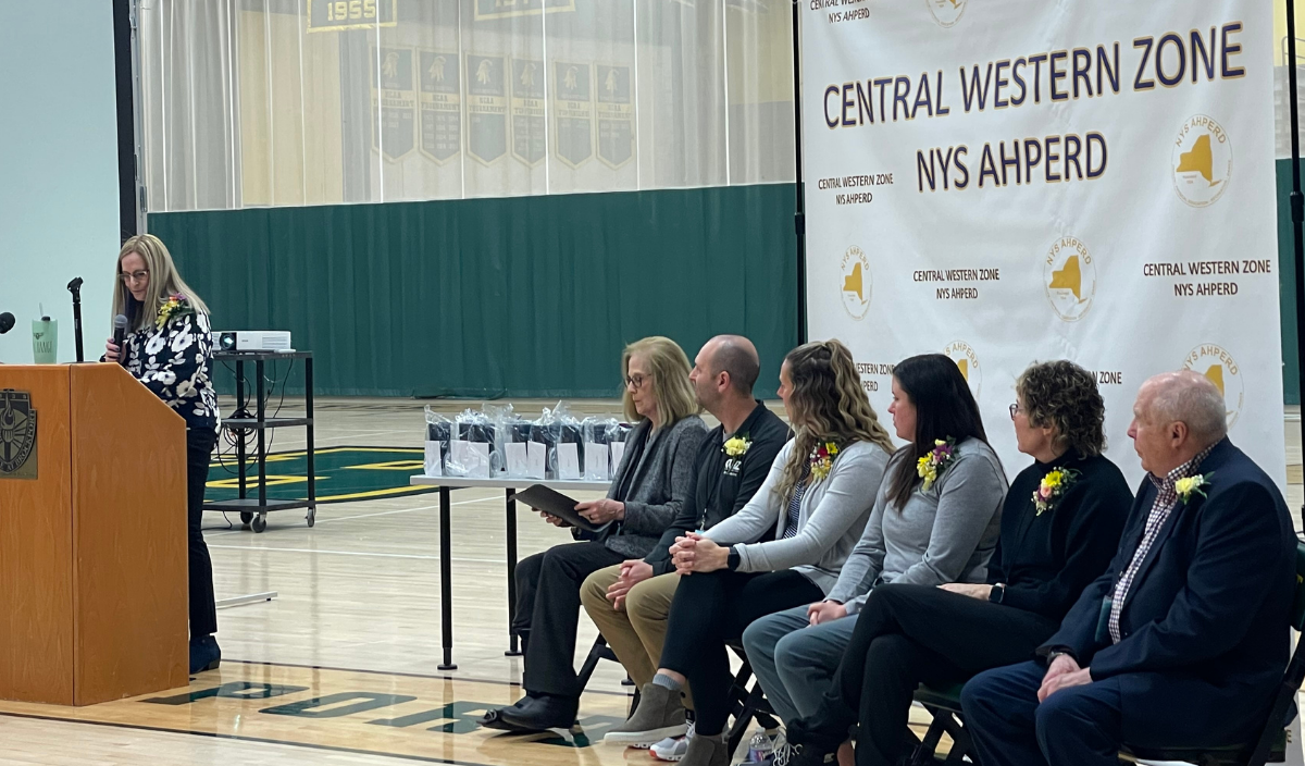 Speaker at podium addressing seated panel at Central Western Zone MS Shaped event in gymnasium