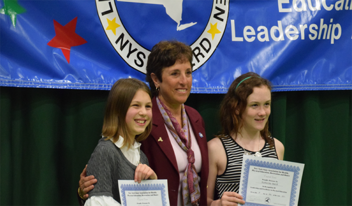 Three people holding certificates in front of a blue banner at an awards ceremony