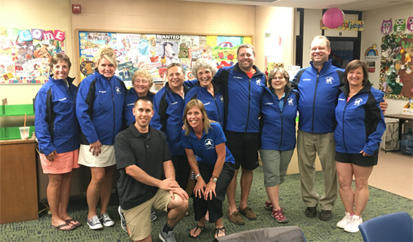 Group of people in blue jackets posing indoors in front of colorful wall art and shelves