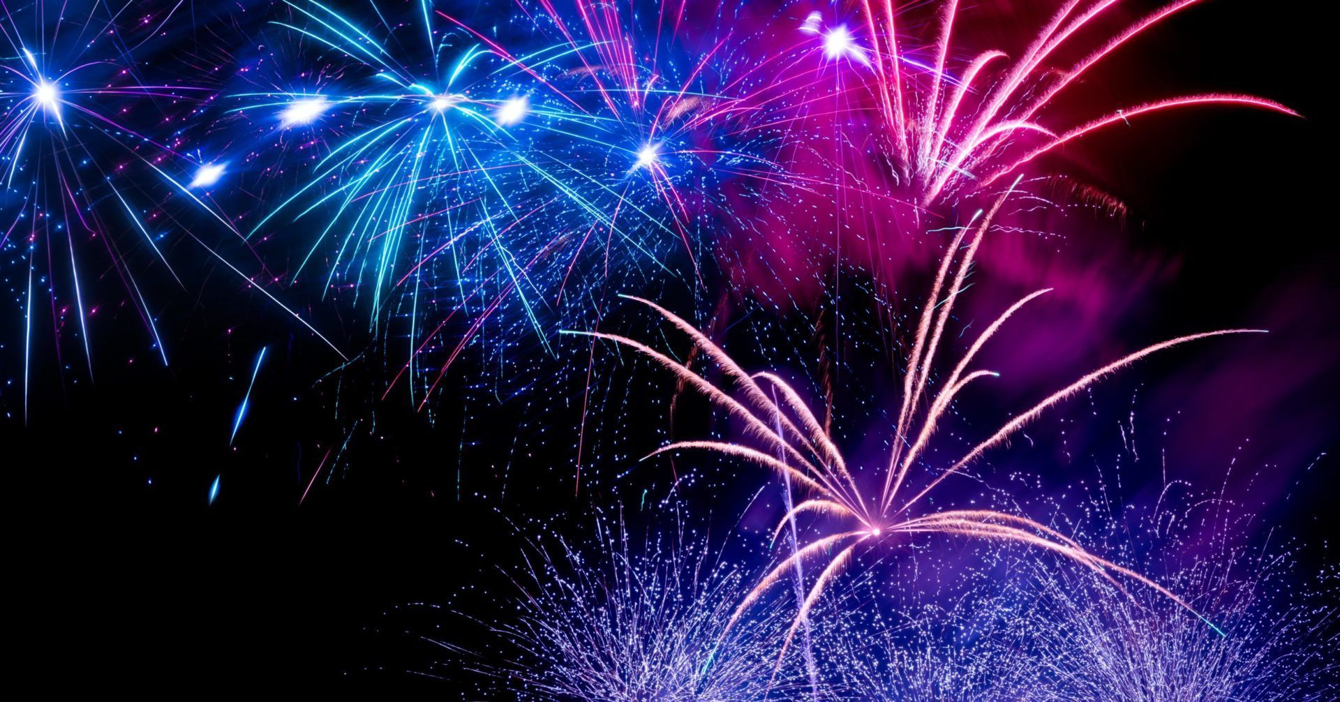 Colorful fireworks bursting in a dark night sky, with blue, pink, and purple sparks