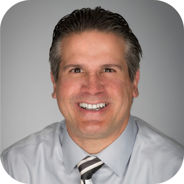 Studio headshot of a smiling man in a light gray shirt and striped tie on a gray background
