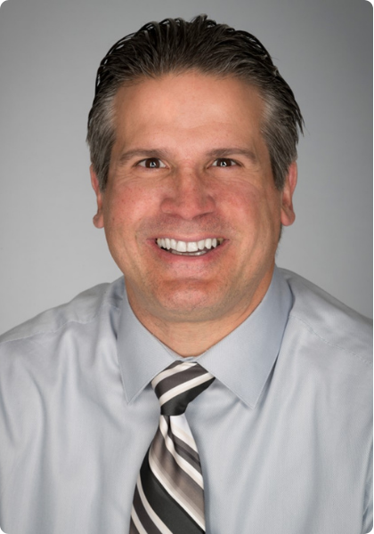 Professional headshot of a smiling person in a light gray shirt and striped tie against a gray background