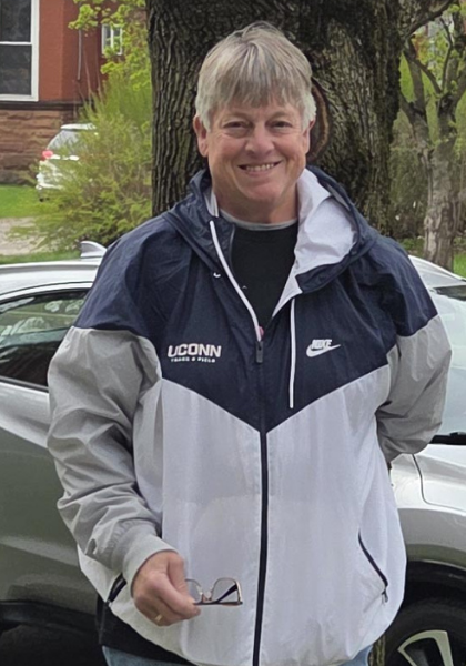 Person smiling in a navy and gray UConn jacket standing outdoors beside a car.