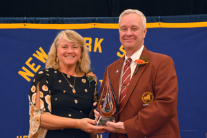 Two people smiling and holding a glass trophy at a New York school event