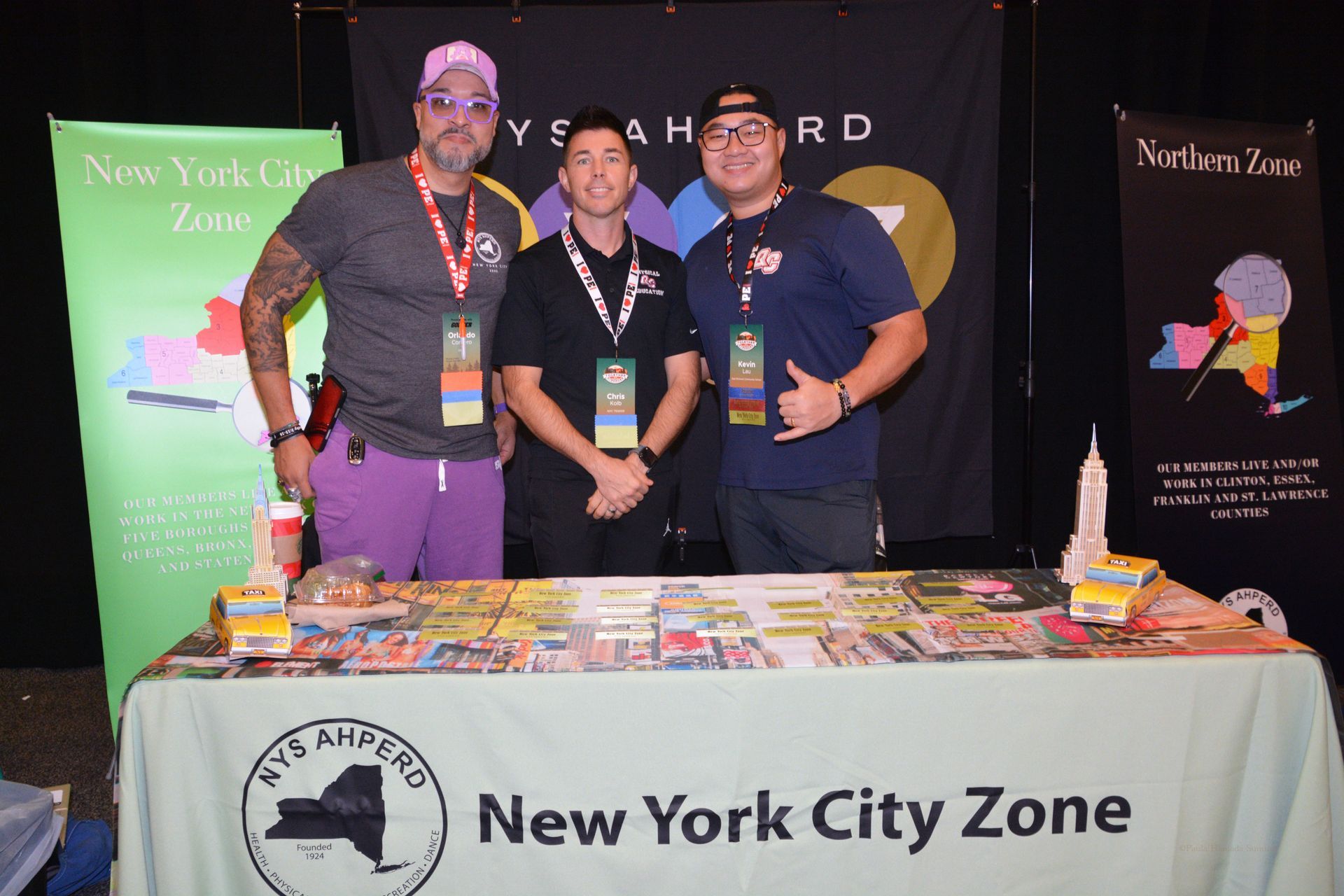Three people posing behind a New York City Zone booth at a convention table
