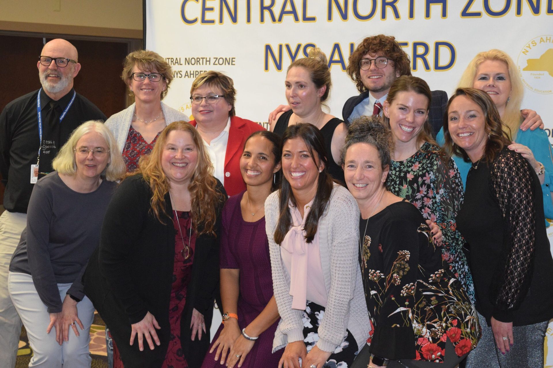 Group of people posing indoors in front of a “Central North Zone NYSAA” sign.