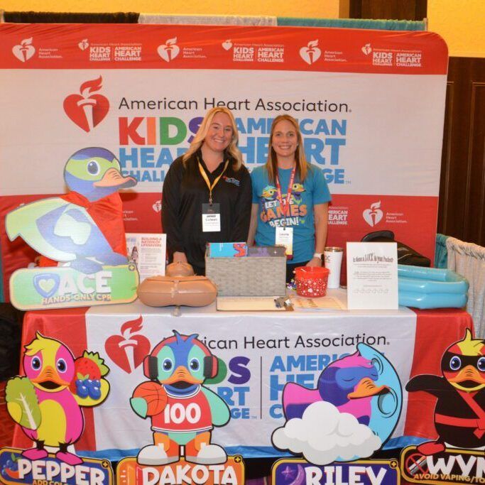 American Heart Association Kids Heart Challenge booth with two women and colorful character cutouts