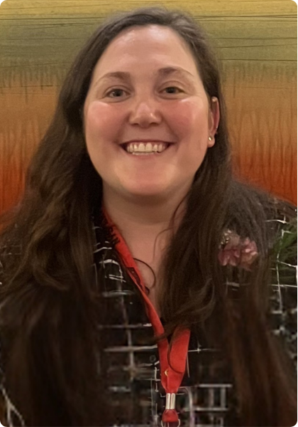 Smiling person with long dark hair wearing a red lanyard, standing before a colorful textured wall.