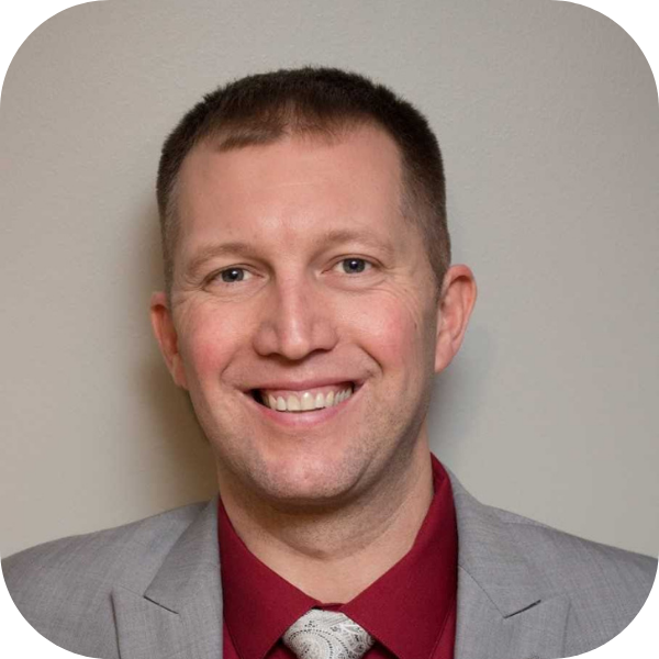 Smiling man in a gray suit and red shirt against a neutral background