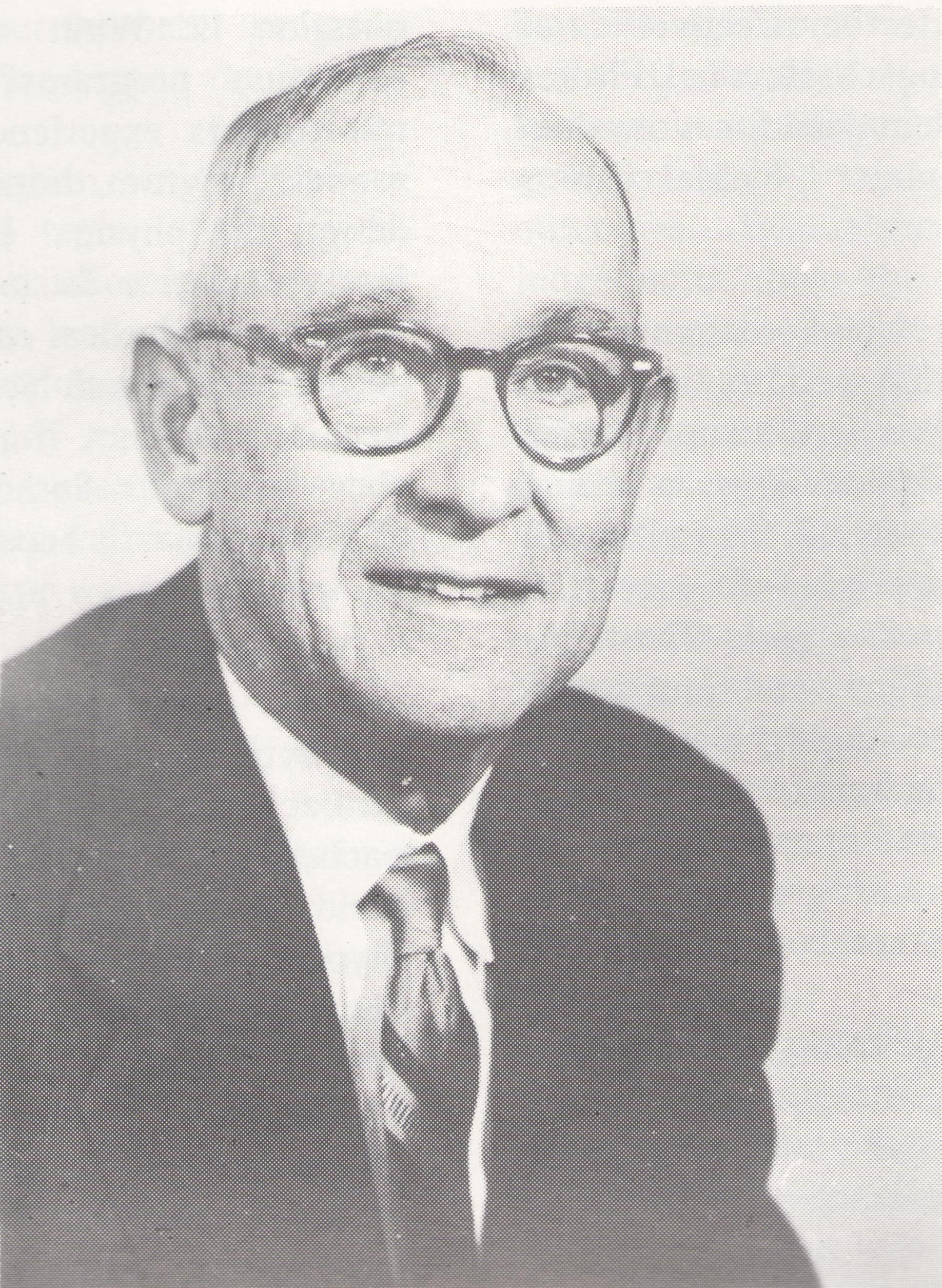 Black-and-white halftone portrait of a man in glasses wearing a suit and tie.