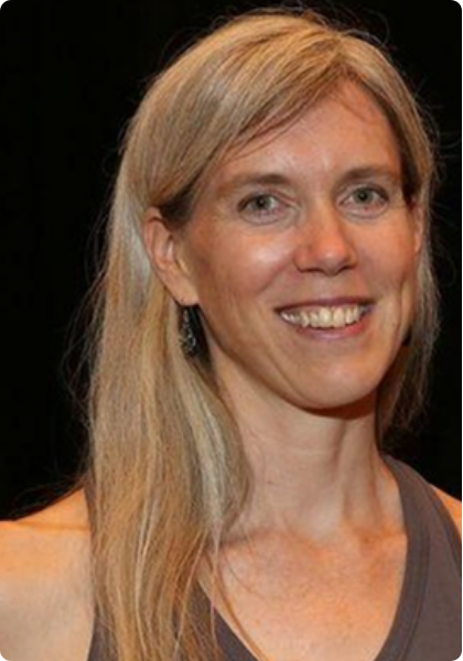 Smiling blonde woman against a black background, wearing a sleeveless top and earrings.