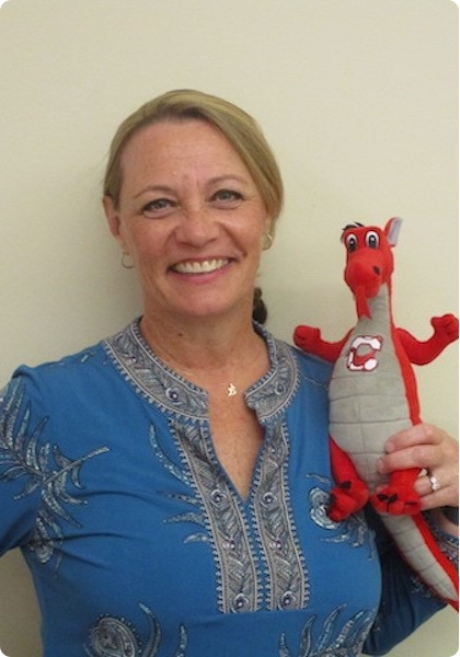 Woman in a blue embroidered blouse smiling and holding a red dragon plush toy