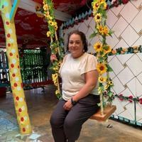 Person sitting on a swing decorated with flowers in a colorful indoor setting, smiling at the camera.