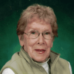 Portrait of a smiling woman with glasses wearing a light green jacket against a green background