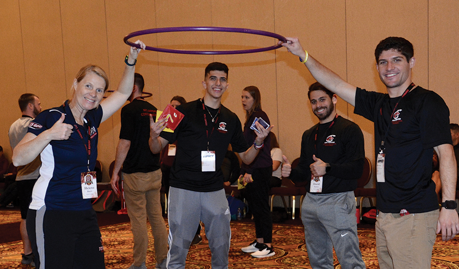 Four people hold a large purple hoop at an indoor event, smiling and posing with lanyards.