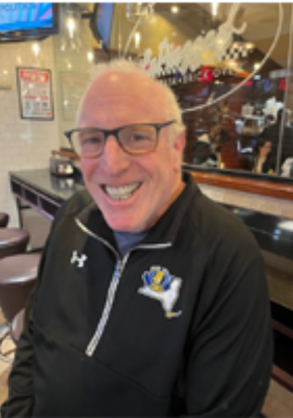 Smiling man in glasses wearing a black zip-up jacket in a restaurant booth