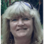 Close-up of a smiling woman with blonde hair outdoors, wearing sunglasses on her head