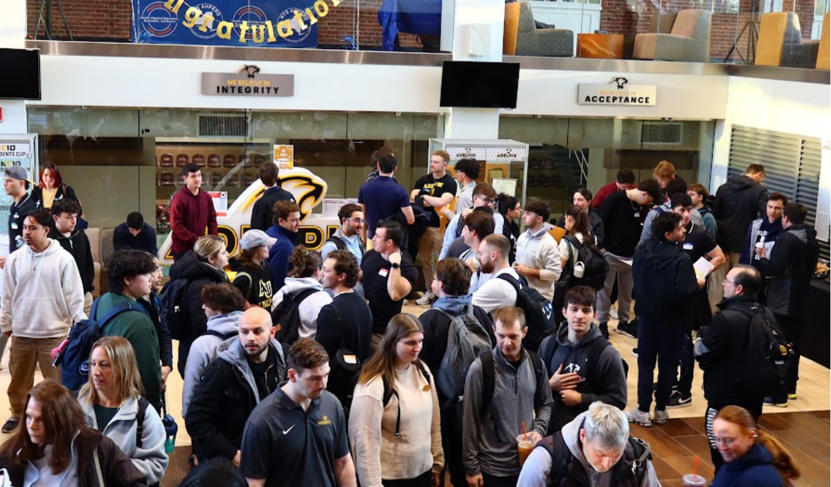 Crowded indoor gathering in a lobby or hall, with people talking and standing beneath signs.