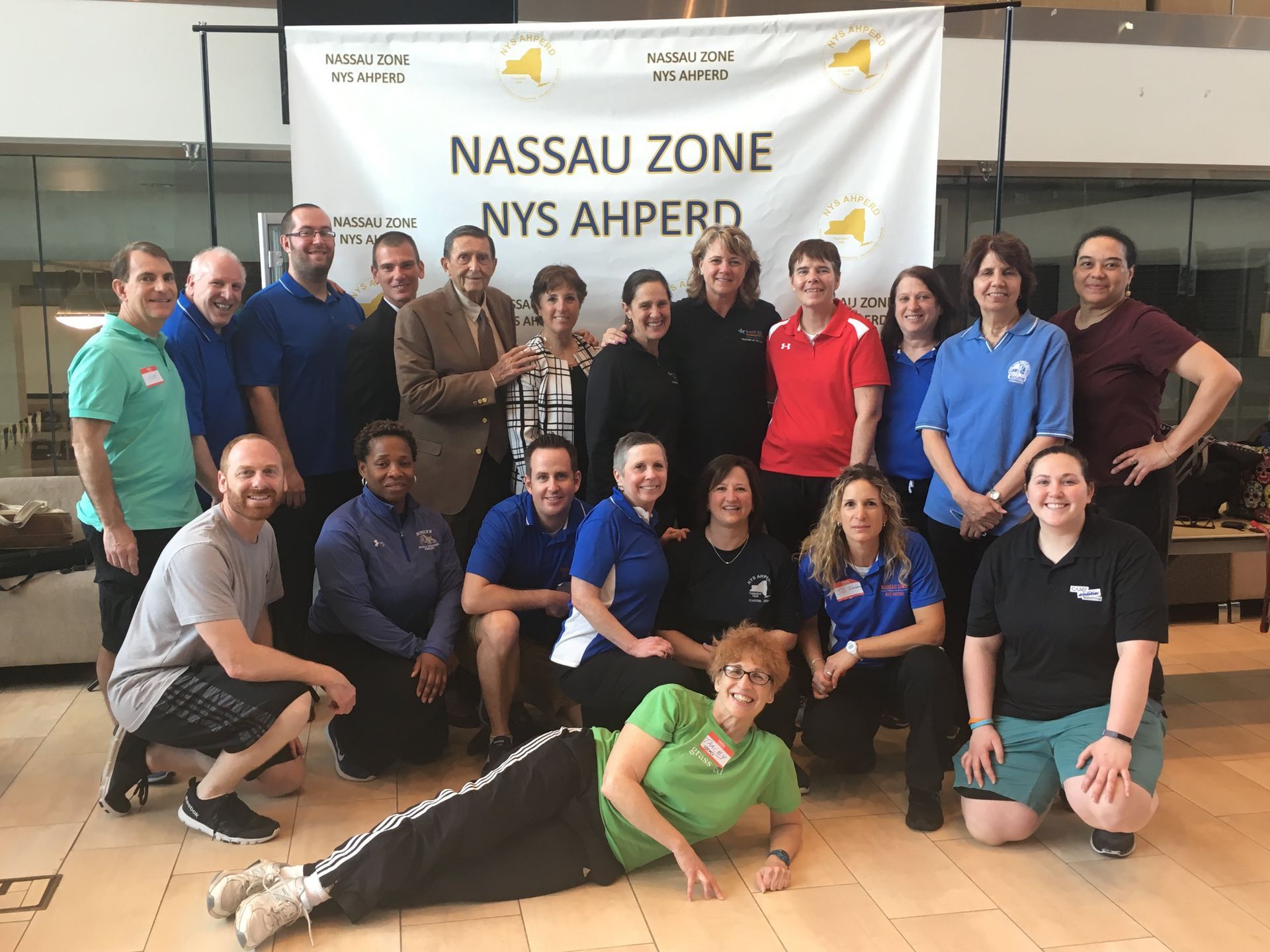 Group of people posing in a gym before a banner reading “Nassau Zone NYS AHPERD”