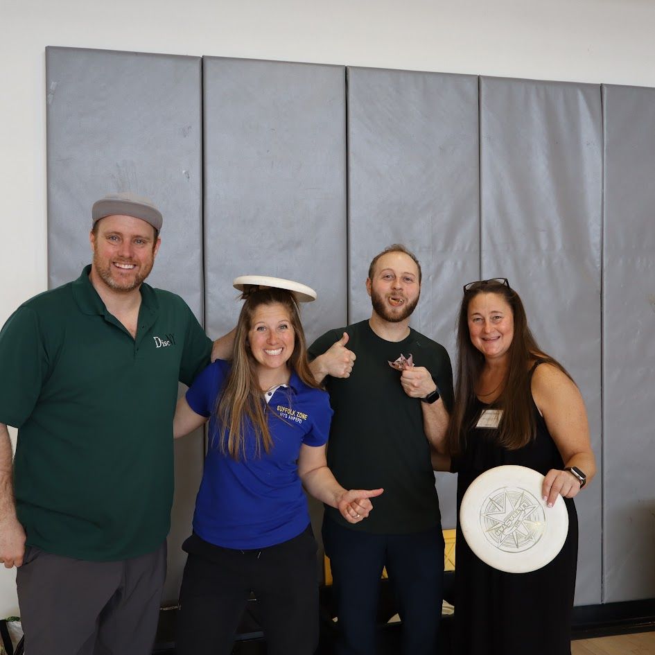 Four people posing indoors, one balancing a plate on her head and another holding a white disc.