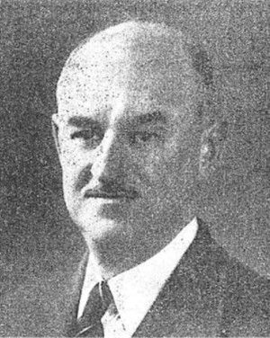 Black-and-white portrait of a man in a suit and tie, facing slightly left with a neutral expression