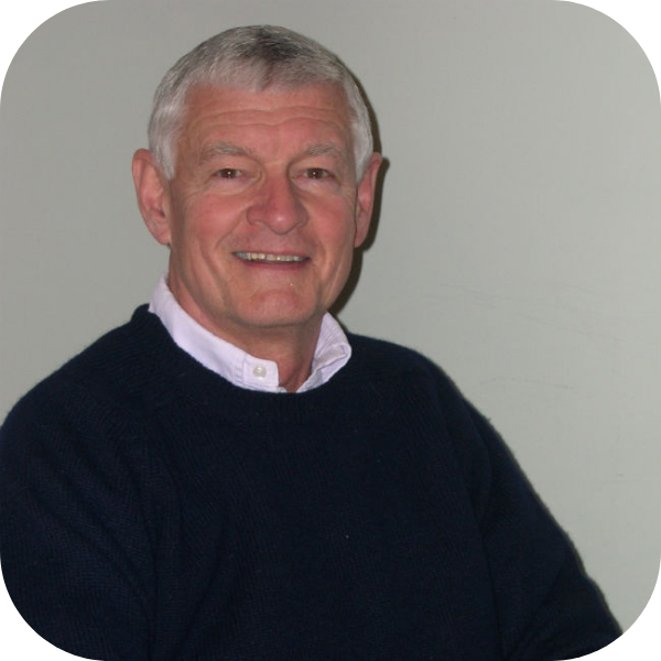 Smiling man in a black sweater over a white collared shirt against a plain gray background