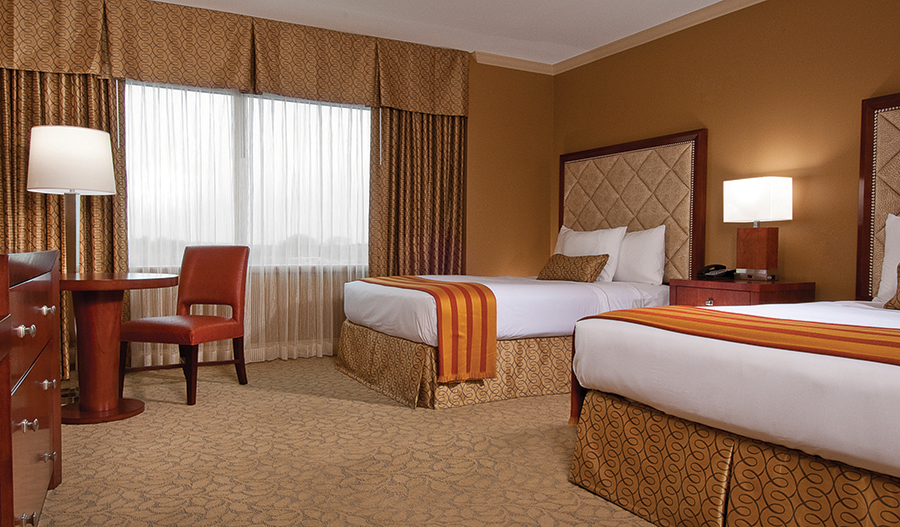 Hotel room with two double beds, desk, lamps, and a window with curtains
