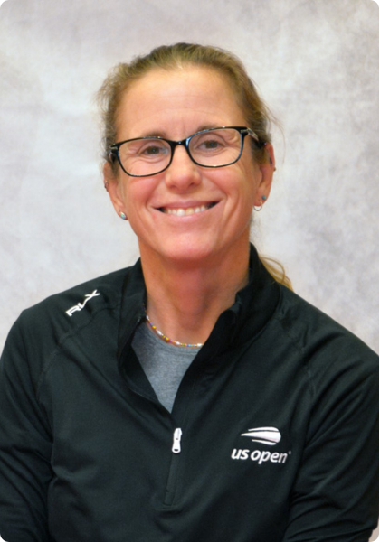 Smiling person in glasses wearing a black US Open jacket against a light gray backdrop