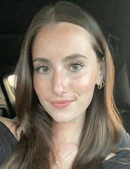 Close-up selfie of a smiling woman with long brown hair, wearing a black top in a car