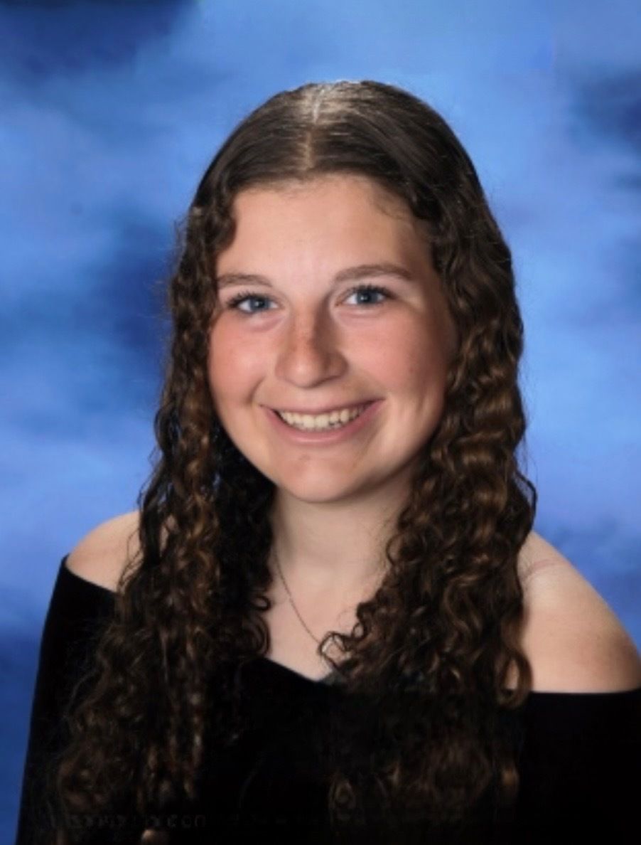 Portrait of a smiling person with long curly brown hair against a blue studio backdrop