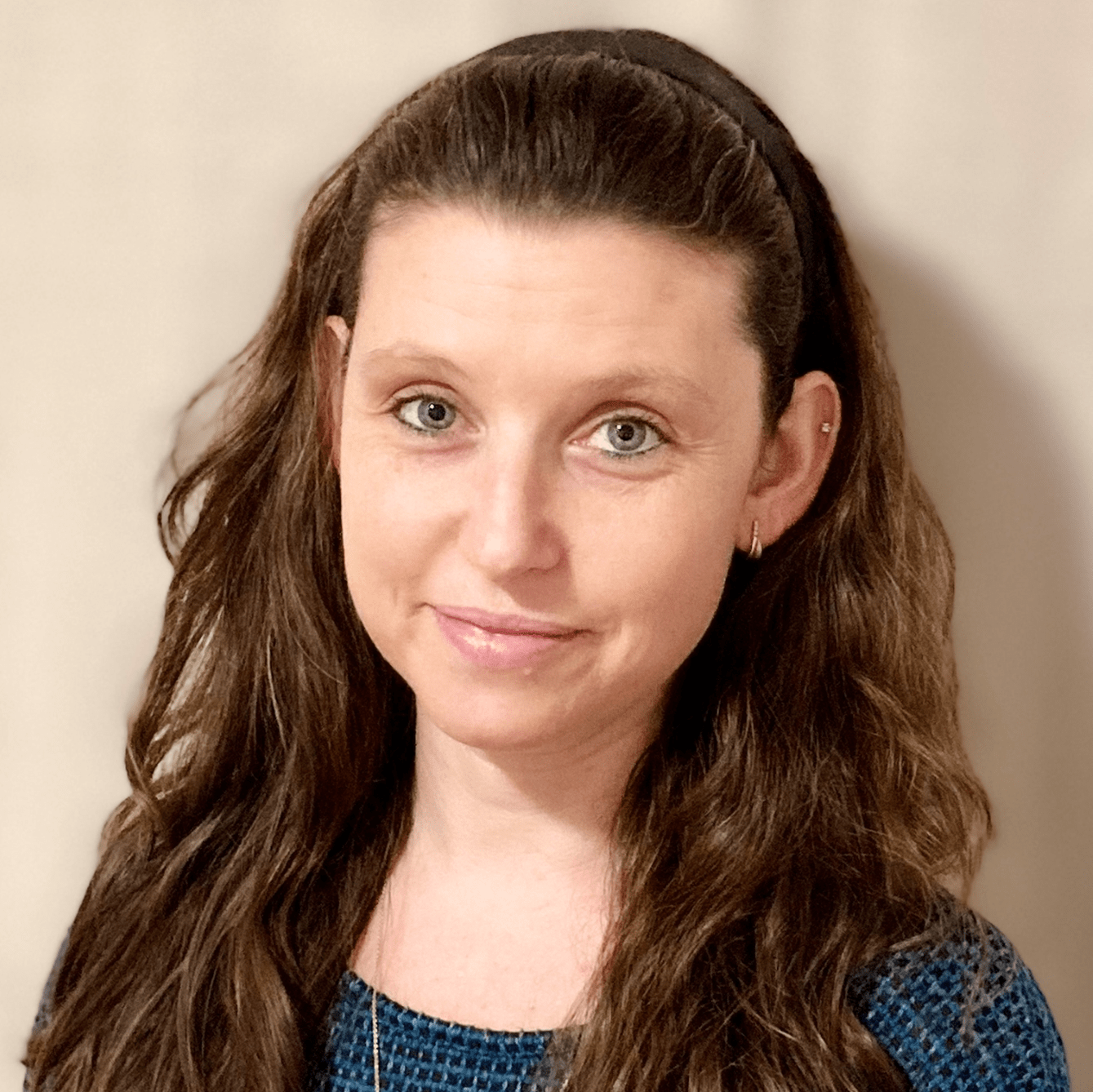 Portrait of a woman with long brown hair wearing a blue top against a beige background
