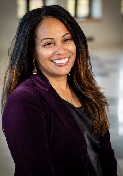 Smiling woman in a purple blazer standing indoors against a blurred background