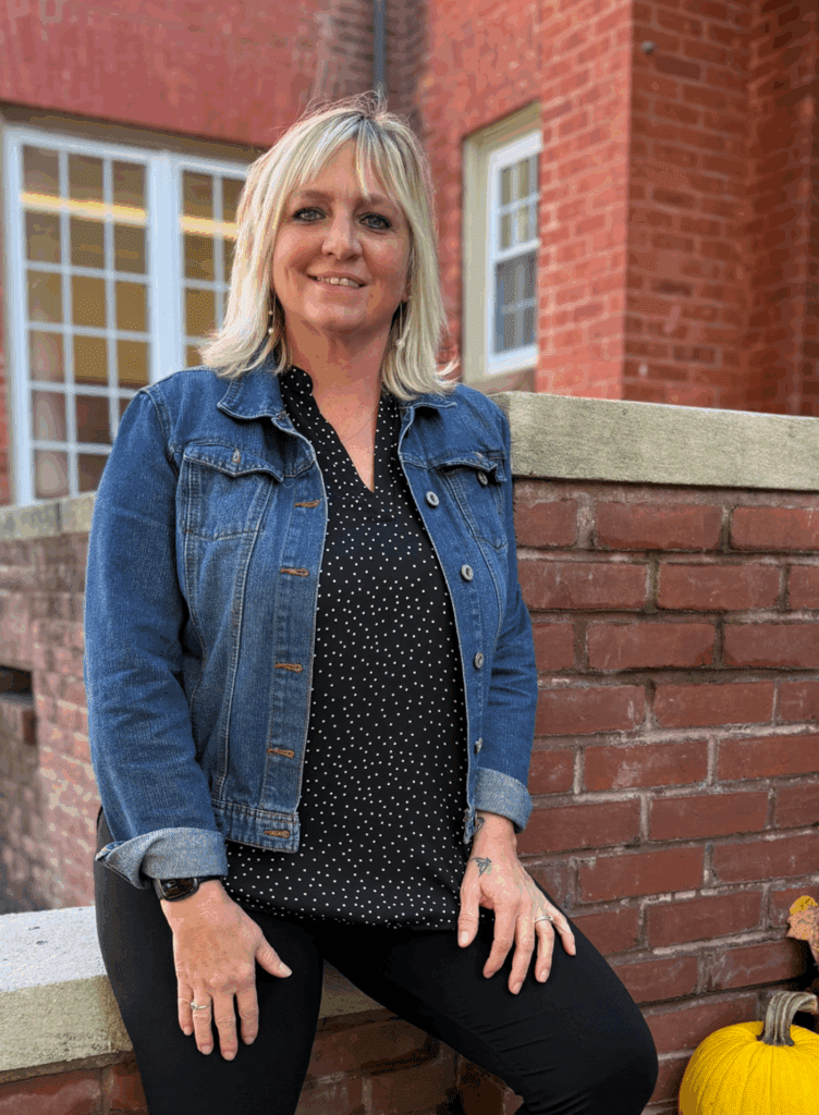 Woman in a denim jacket posing by a brick wall outside a building