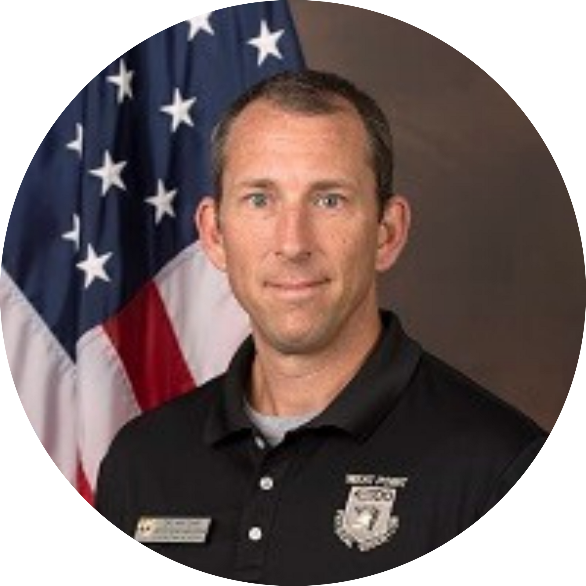 Portrait of a man in a black polo shirt standing before a U.S. flag backdrop