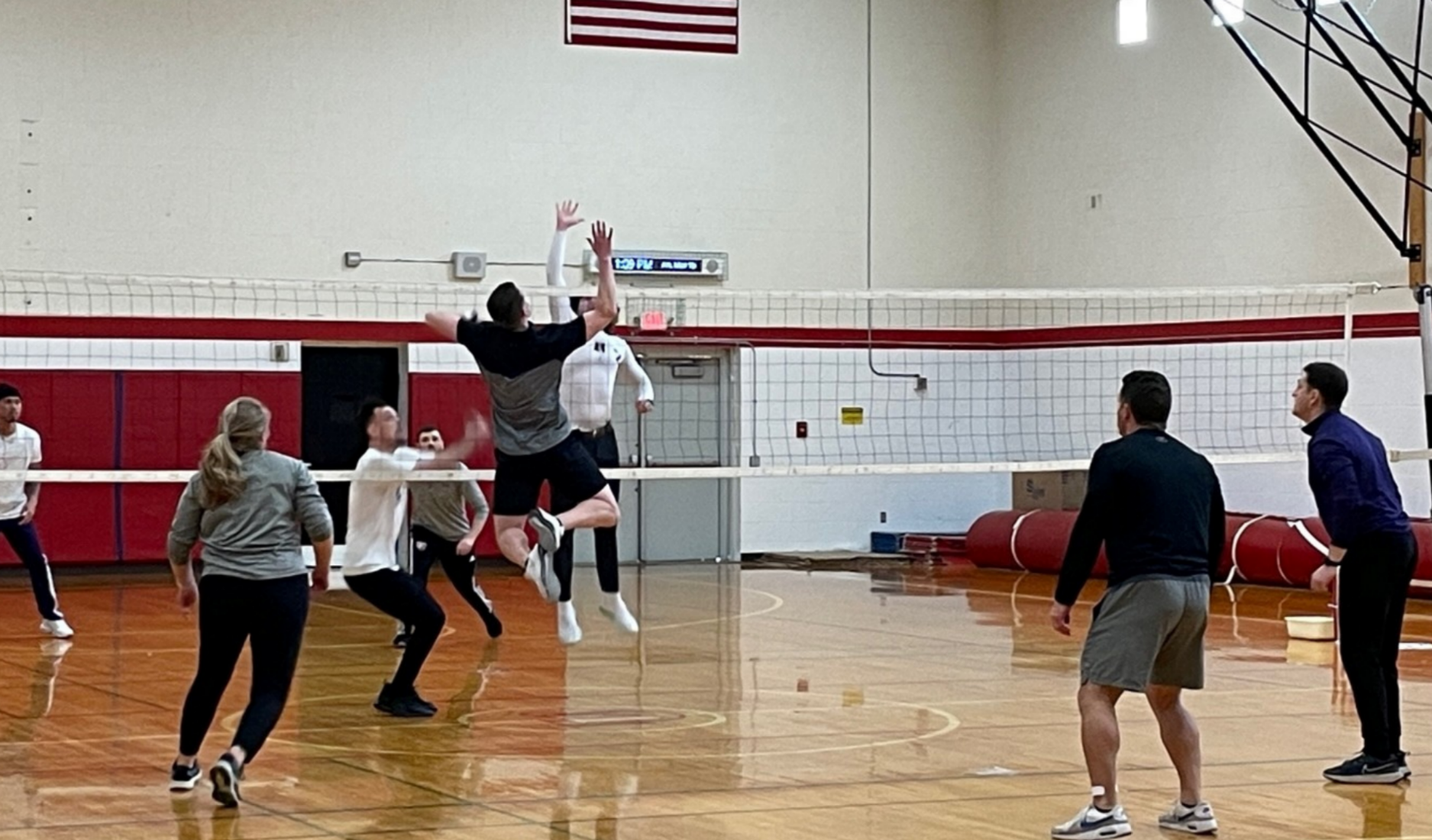 Indoor volleyball game with players jumping at the net in a gymnasium