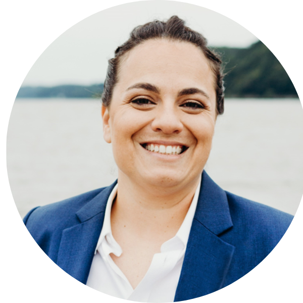 Smiling person in a blue blazer outdoors by the water